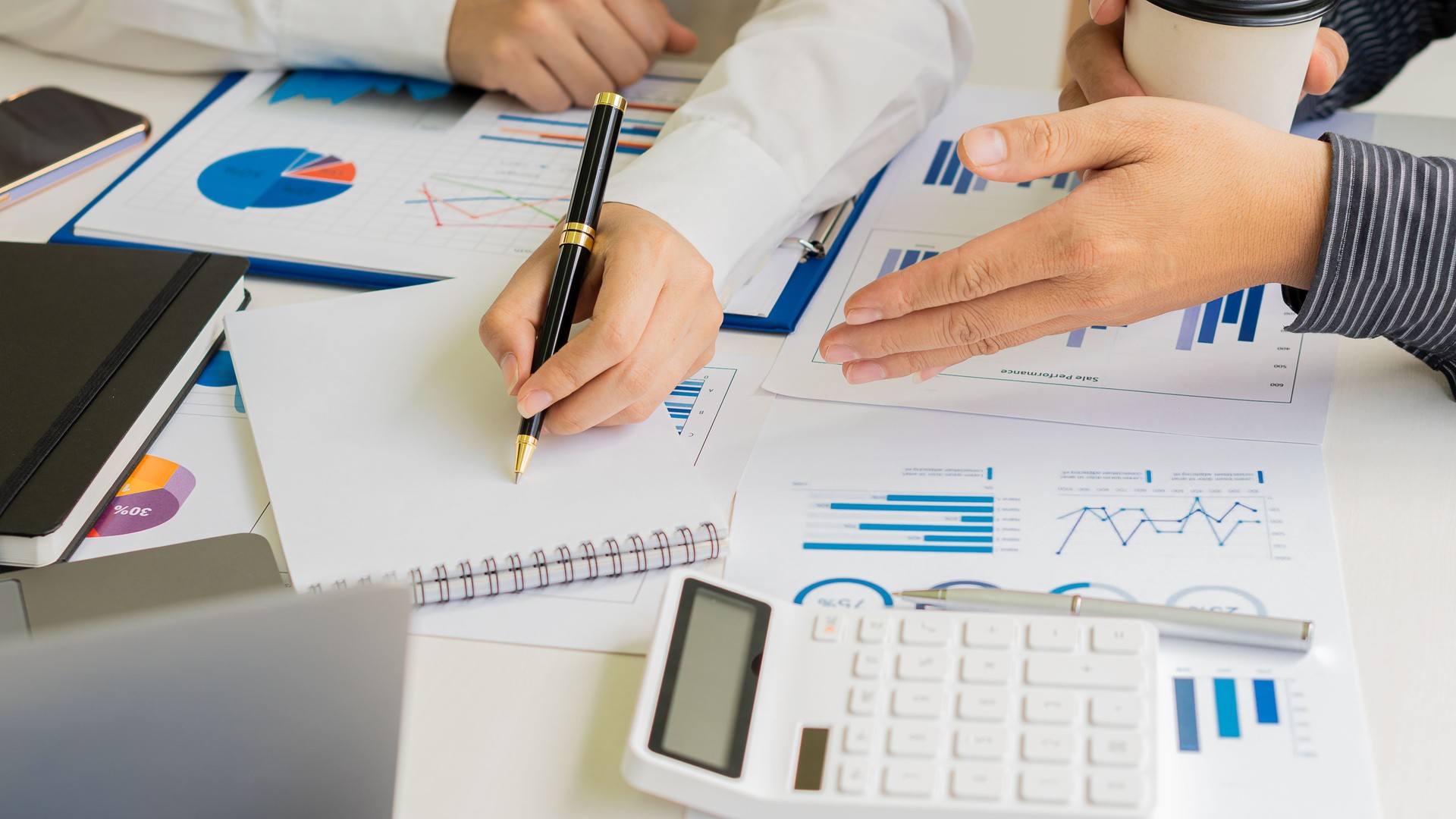 Groupe d’hommes d’affaires tenant un stylo intelligent discutant lors d’une réunion de groupe à table dans un bureau moderne avec des papiers millimétrés et un ordinateur portable Planification stratégique, collaboration commerciale et brainstor